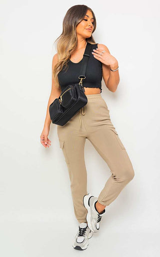 Woman wearing beige cargo pocket trouser with drawstring, black top, and white sneakers.