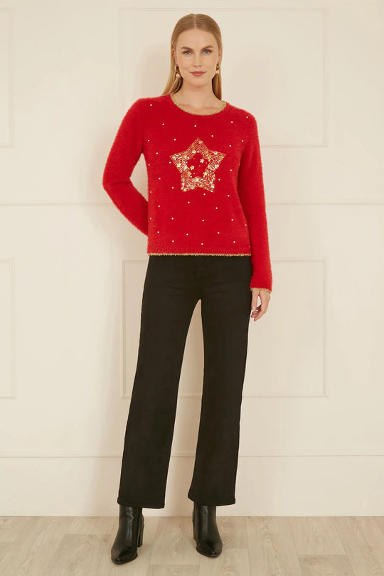 Woman wearing red knitted fluffy Christmas star jumper with gold embellishments paired with black pants and boots