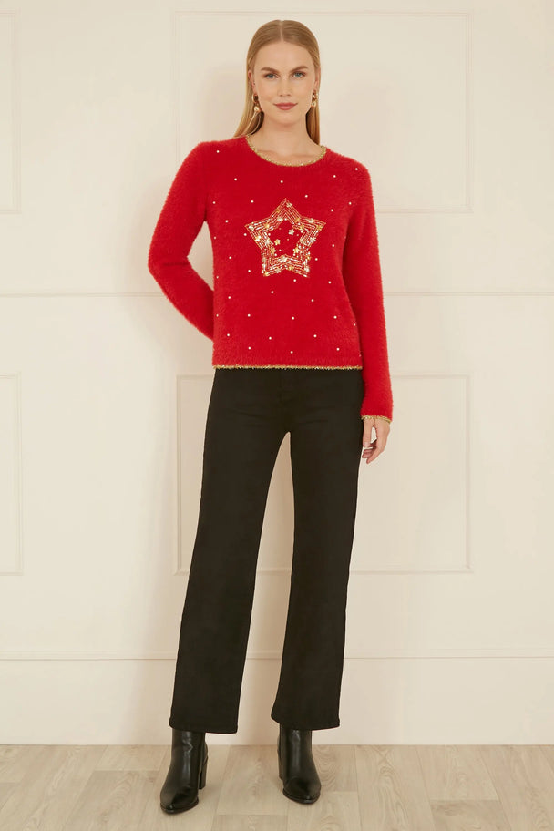 Woman wearing red knitted fluffy Christmas star jumper with gold embellishments paired with black pants and boots