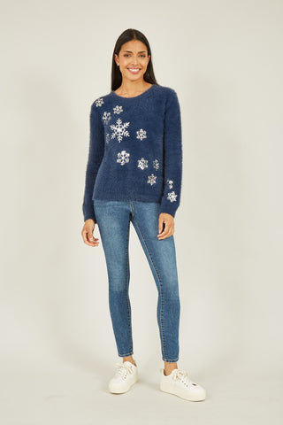 Woman wearing navy sequin snowflake fluffy jumper with silver snowflake embellishments and blue jeans