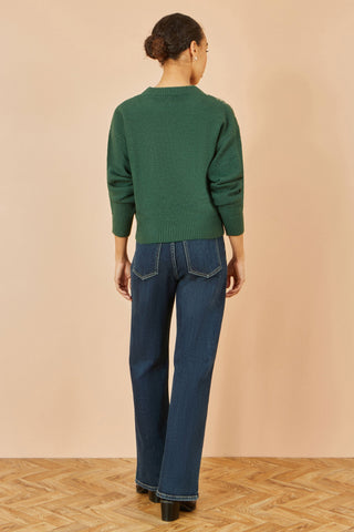 Woman wearing green relaxed knitted jumper with scattered sequins on neckline and blue jeans, back view