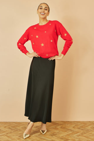 Woman wearing red gold foil star print relaxed fit jumper with black skirt and gold shoes